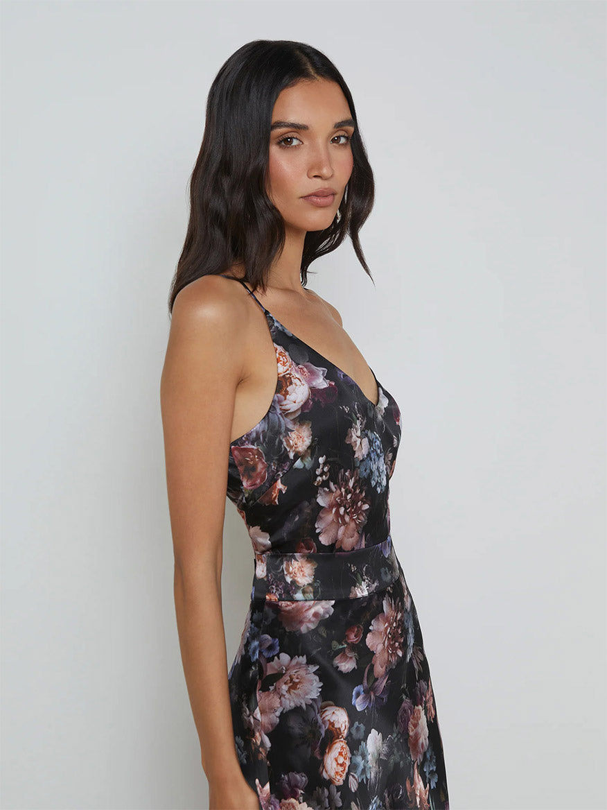 A person wearing the L'Agence Gabriella Silk Camisole in Black Multi Vintage Oil Flower, featuring a floral print with delicate adjustable straps, stands against a plain background.