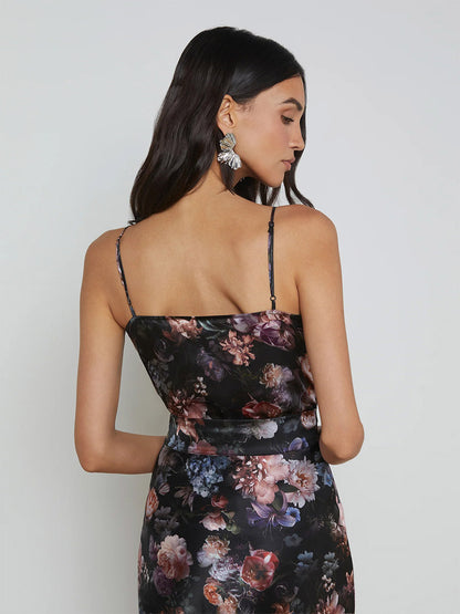 A woman with long dark hair is wearing the L'Agence Gabriella Silk Camisole in Black Multi Vintage Oil Flower, featuring adjustable straps, as she faces away from the camera.