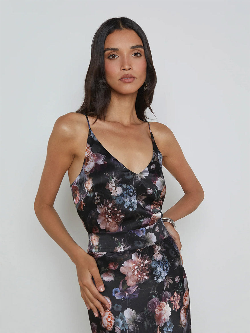 A woman wearing the L'Agence Gabriella Silk Camisole in Black Multi Vintage Oil Flower stands against a plain background, highlighting the delicate floral print on the garment.