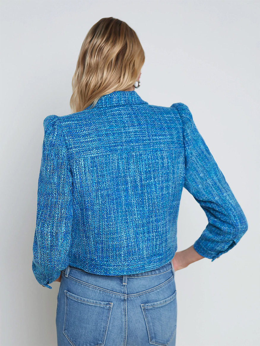 Woman viewed from behind, named Kasey, wearing a L'Agence Kasey Tweed Jacket in Caribbean Blue Multi Tweed and blue jeans against a white background.