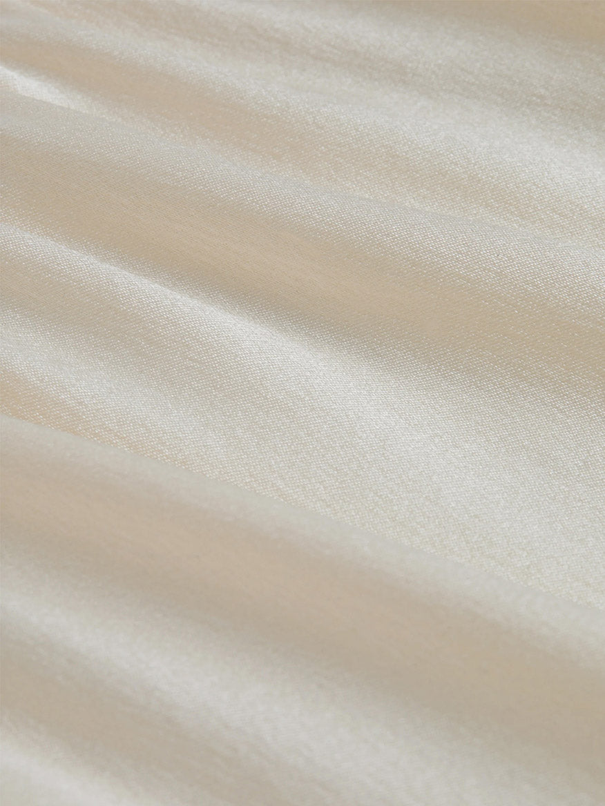 Close-up of smooth, cream-colored satin fabric with a subtle sheen and gentle folds, perfect for an elegant L'Agence Lexi Silk Camisole in Ivory.