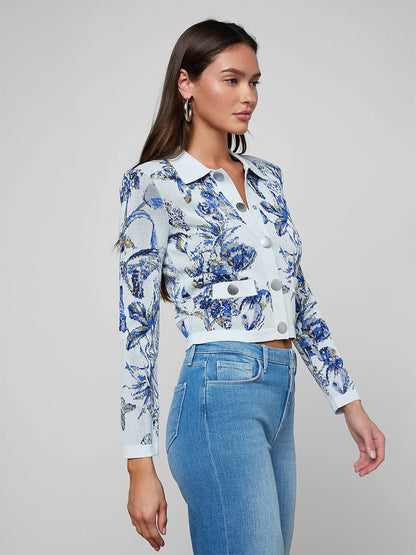 A woman in profile wears the L'Agence Osiris Jacquard Cardigan in Grey Multi Watercolor Butterfly Jacquard with blue jeans, standing against a plain background.