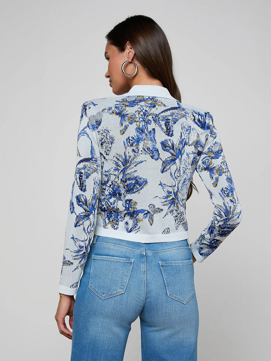 A woman facing away wears the L'Agence Osiris Jacquard Cardigan in Grey Multi Watercolor Butterfly Jacquard with blue jeans and large hoop earrings.