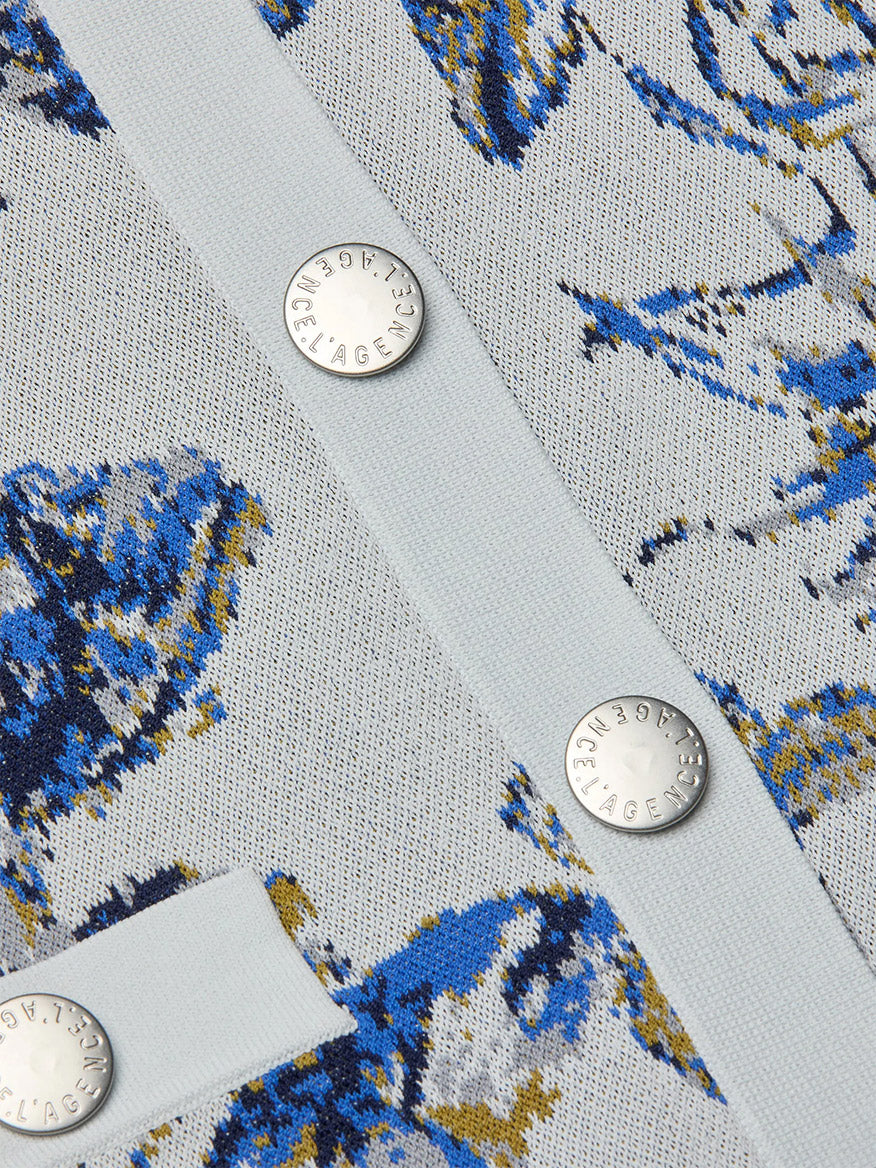Close-up of the L'Agence Osiris Jacquard Cardigan in Grey Multi Watercolor Butterfly Jacquard, showcasing textured fabric with a blue and yellow abstract pattern and three silver snap buttons engraved with "L'Agence.