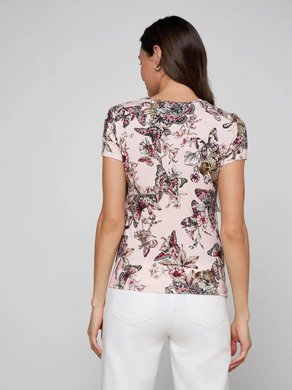A woman with long brown hair, facing away from the camera against a plain background, wears white pants and the bestselling L'Agence Ressi Fitted Tee in Nectar Pink Multi Butterfly Jungle.