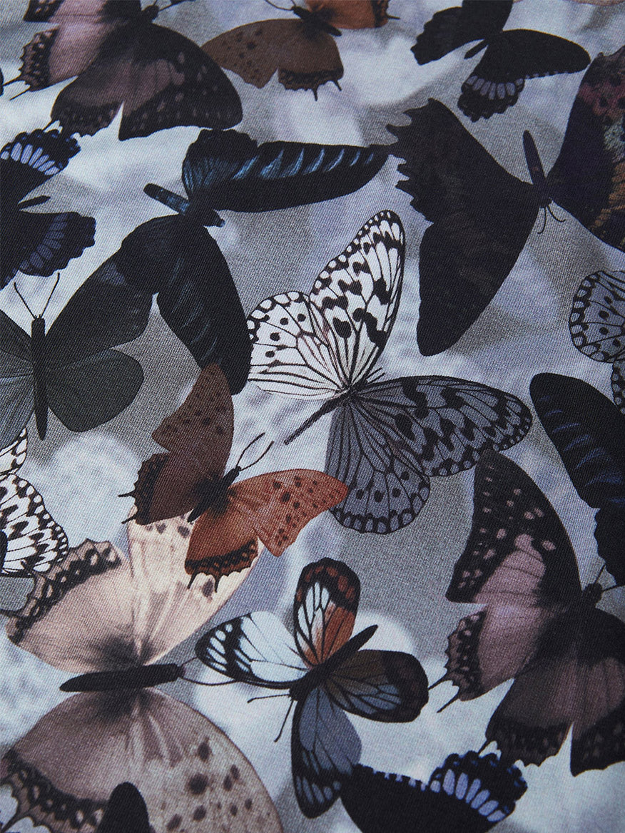 A collection of butterfly silhouettes and patterns adorns the L'Agence Ressi Short Sleeve Crew in Multi Dark Butterfly, showcasing hues of black, white, brown, and blue. Crafted in Los Angeles, its vivid butterfly design adds a fashionable flair.