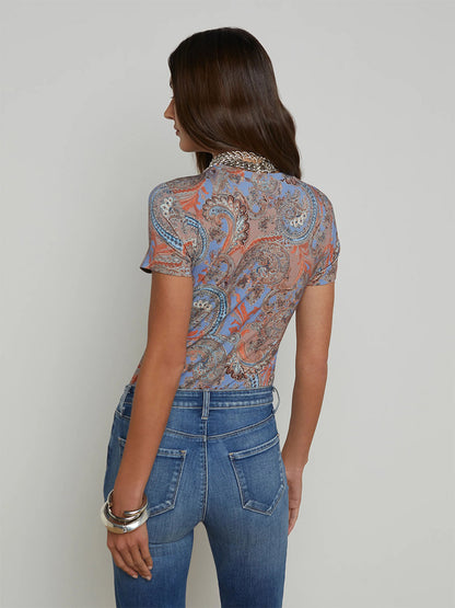 A woman with long hair, wearing the L'Agence Ressi Fitted Tee in Periwinkle Multi French Paisley and jeans, stands facing away from the camera.