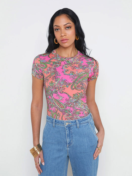 A woman in a L'Agence Ressi Fitted Tee in Small Rhodamine Pop Paisley and blue jeans standing against a white background.