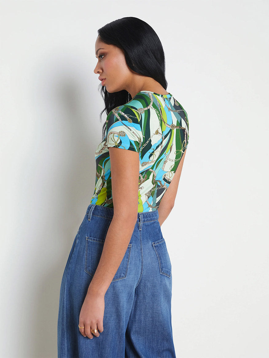 A woman in profile wears a L'Agence Ressi Fitted Tee in Small Sea Green Belt Swirl and blue jeans against a neutral background. Her hair is straight and black.
