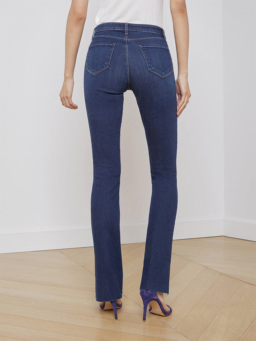 Rear view of a woman wearing L'Agence Ruth High Rise Straight Relaxed Jeans in Venus and purple high heels standing on a wooden floor.