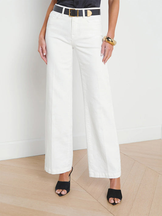 A person wearing L'Agence Scottie Wide-Leg Jeans in Blanc and black open-toed heels stands on a wooden floor against a plain background.