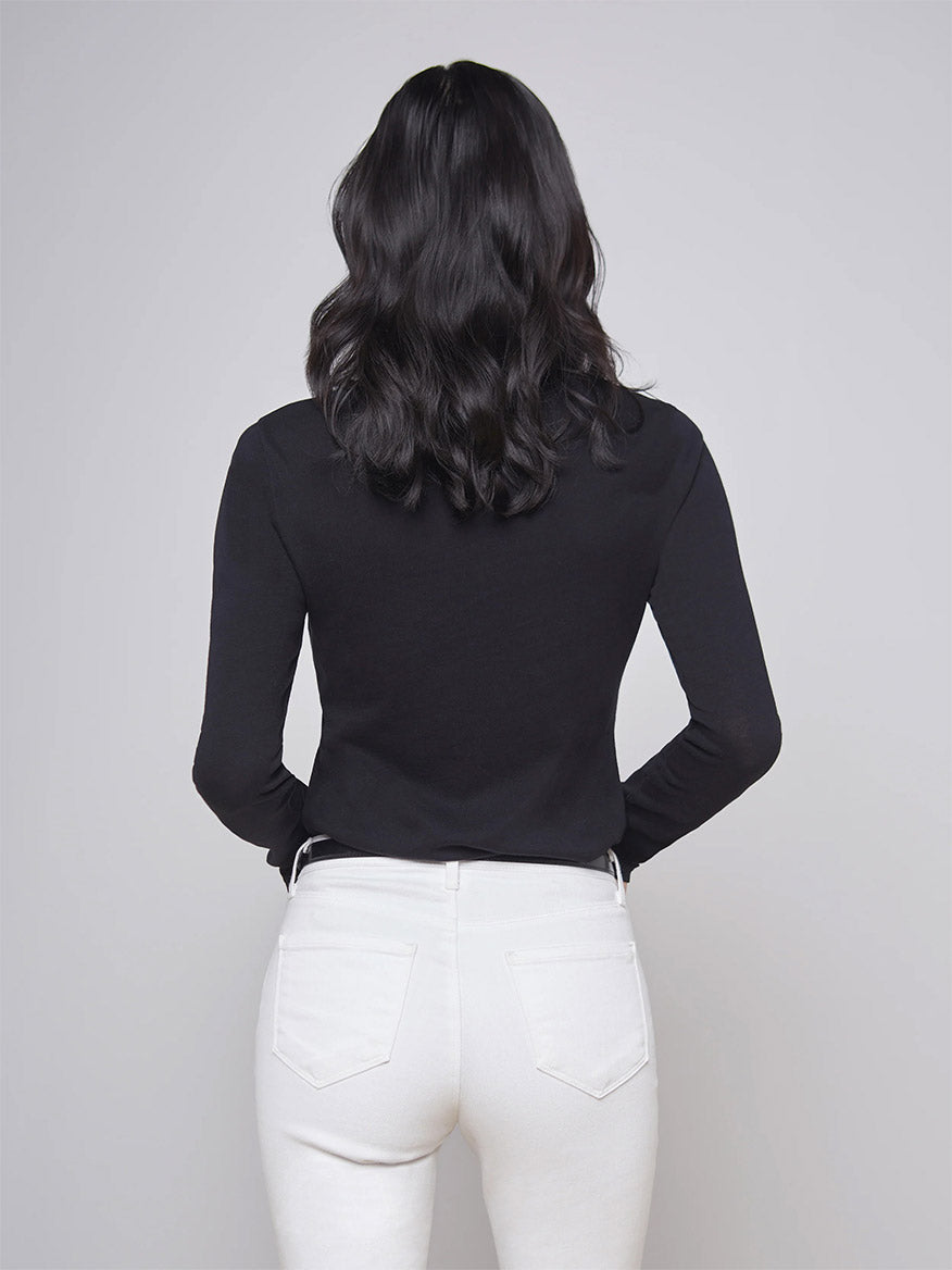 A woman with long black hair is facing away, wearing the form-fitting L'Agence Tess Long Sleeve Crew in Black and white pants.