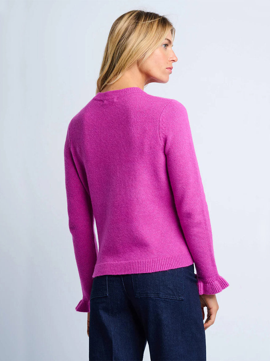 A person with long blonde hair wears the Lisa Todd Allure Henley in Hot Orchid with dark blue jeans, standing and looking to the side against a plain light background.