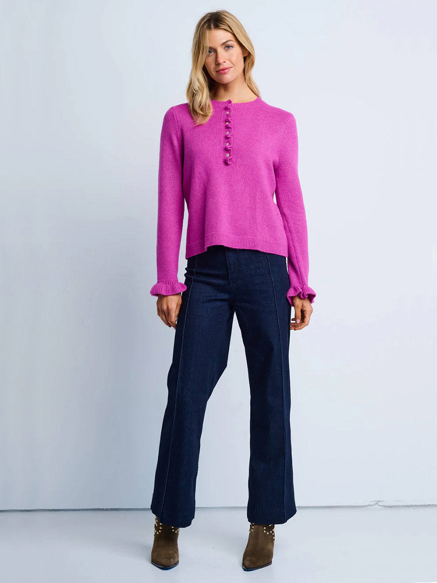 A person wears the Lisa Todd Allure Henley in Hot Orchid, dark wide-leg recycled jeans, and brown ankle boots, standing against a plain light background.