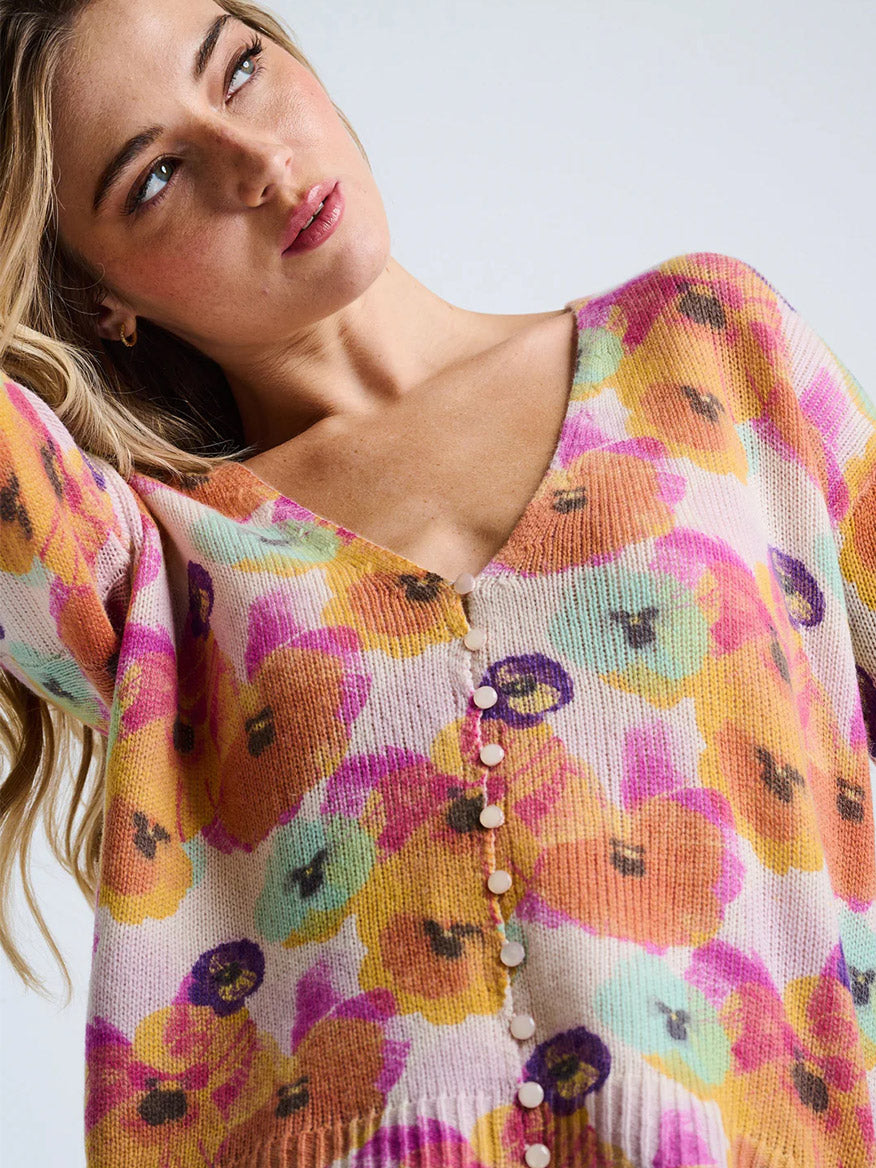 A woman models the Lisa Todd Bloomin' Cardigan in Frost Combo, a colorful, floral wool-cashmere blend sweater with a relaxed fit and V-neckline, set against a plain background.