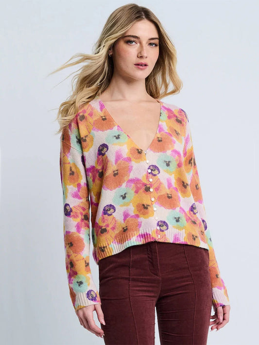 A woman wears the Lisa Todd Bloomin' Cardigan in Frost Combo, a relaxed-fit V-neck floral sweater, paired with maroon corduroy pants, standing against a plain light background.