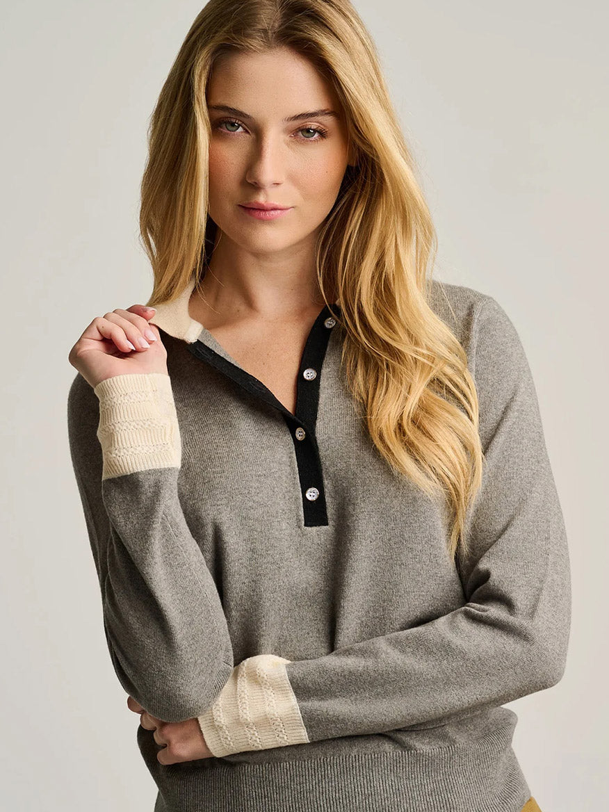 A person with long blonde hair wears the Lisa Todd Pop Posh Cotton Cashmere Polo in Grey Shadow, a sophisticated pullover featuring cream-colored cuffs and collar, standing against a plain background.