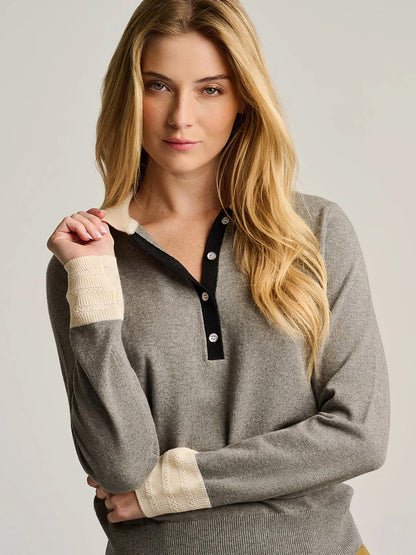 A person with long blonde hair wears the Lisa Todd Pop Posh Cotton Cashmere Polo in Grey Shadow, a sophisticated pullover featuring cream-colored cuffs and collar, standing against a plain background.