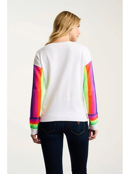A woman faces away, wearing the Lisa Todd Brite Side Cotton Sweater in White—a knit pullover with rainbow stripes—and dark jeans against a plain background.