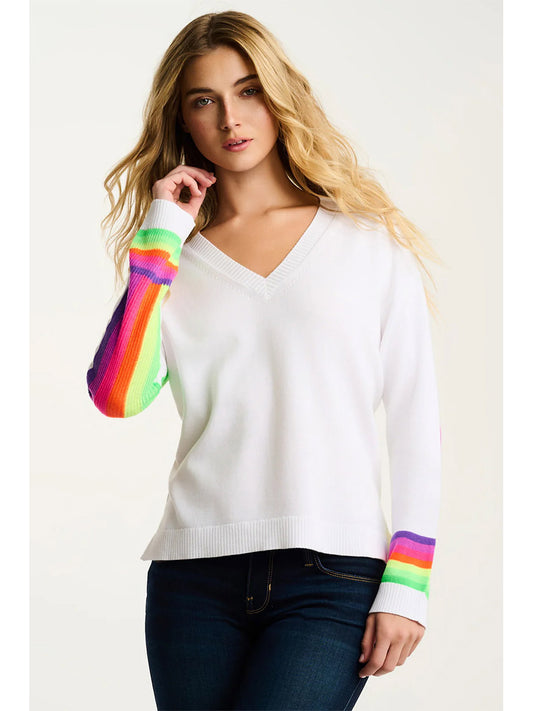 A person wearing the Lisa Todd Brite Side Cotton Sweater in White with rainbow-striped sleeves and dark blue jeans stands against a plain background.