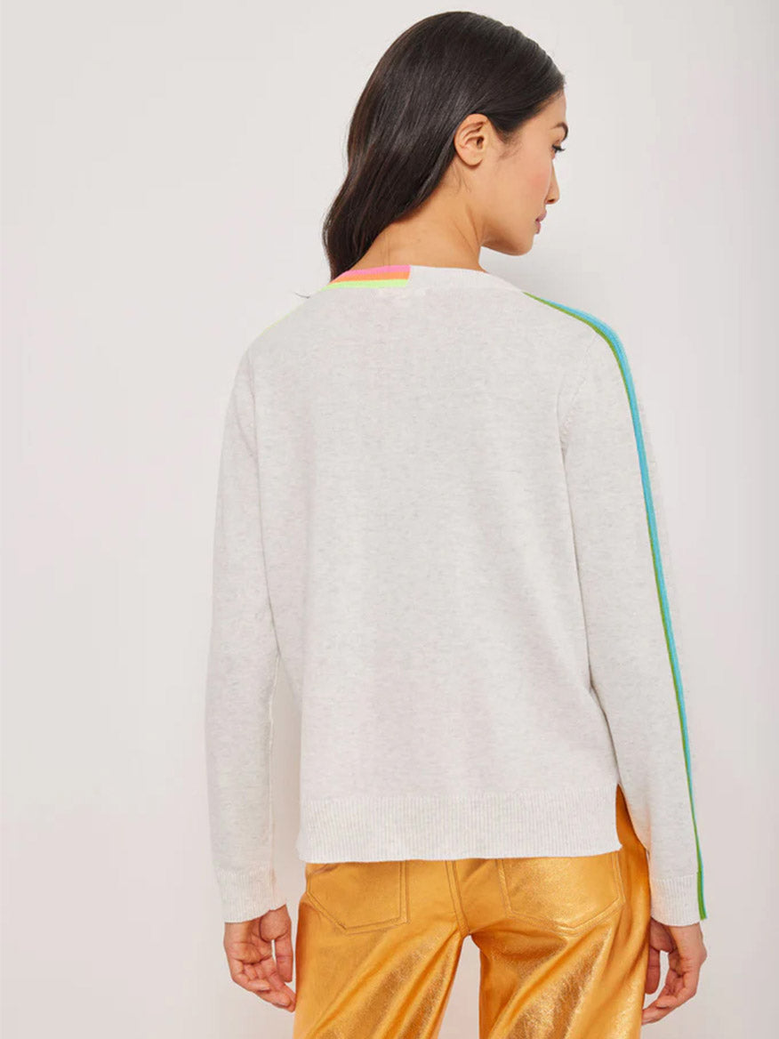 Woman wearing a light grey v-neck Lisa Todd Color Code sweater in Mineral with colored trim detail, part of the Lisa Todd spring wardrobe, paired with metallic gold pants, viewed from the back.