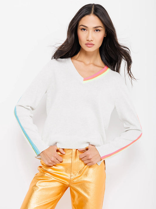 Woman posing in a Lisa Todd Color Code Sweater in Mineral, featuring a v-neck white sweater with colorful trim and shiny gold pants.