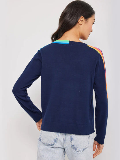 Woman wearing a Lisa Todd Color Code Sweater in Navy with a rainbow stripe detail on the sleeves and shoulders, viewed from the back, perfect for refreshing your spring wardrobe.