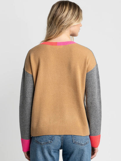A person with long blonde hair, facing away from the camera, wears the Lisa Todd Color Wheel Sweater in Fog/Caramel—featuring a relaxed fit and colorblock design—paired with blue jeans.