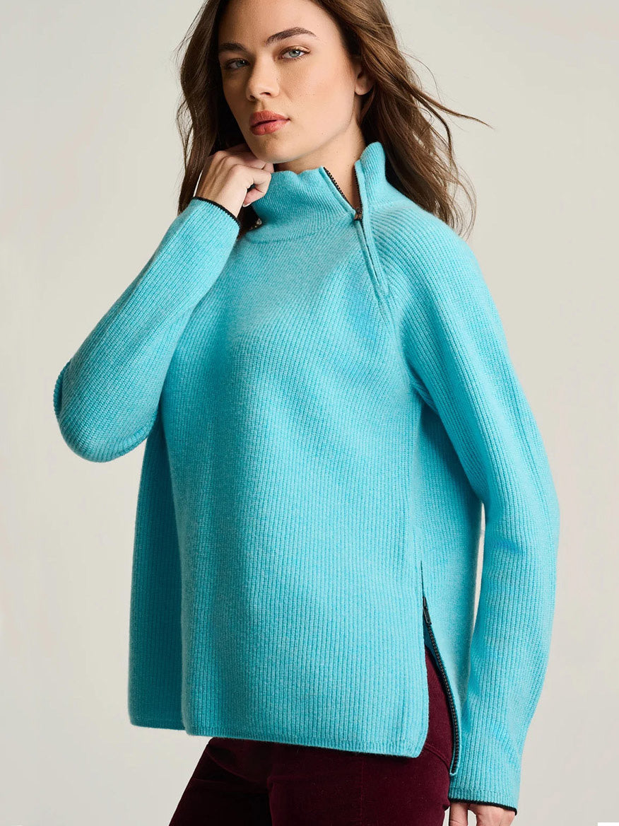 A woman wears a bright blue Lisa Todd Double Trouble Cashmere Sweater featuring a rib-stitched funnel neck with a contrast zip and side slits.