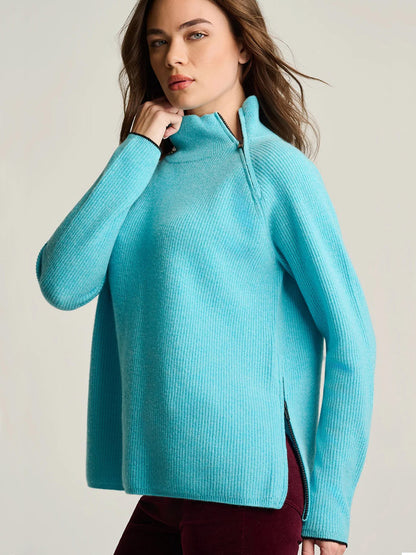 A woman wears a bright blue Lisa Todd Double Trouble Cashmere Sweater featuring a rib-stitched funnel neck with a contrast zip and side slits.