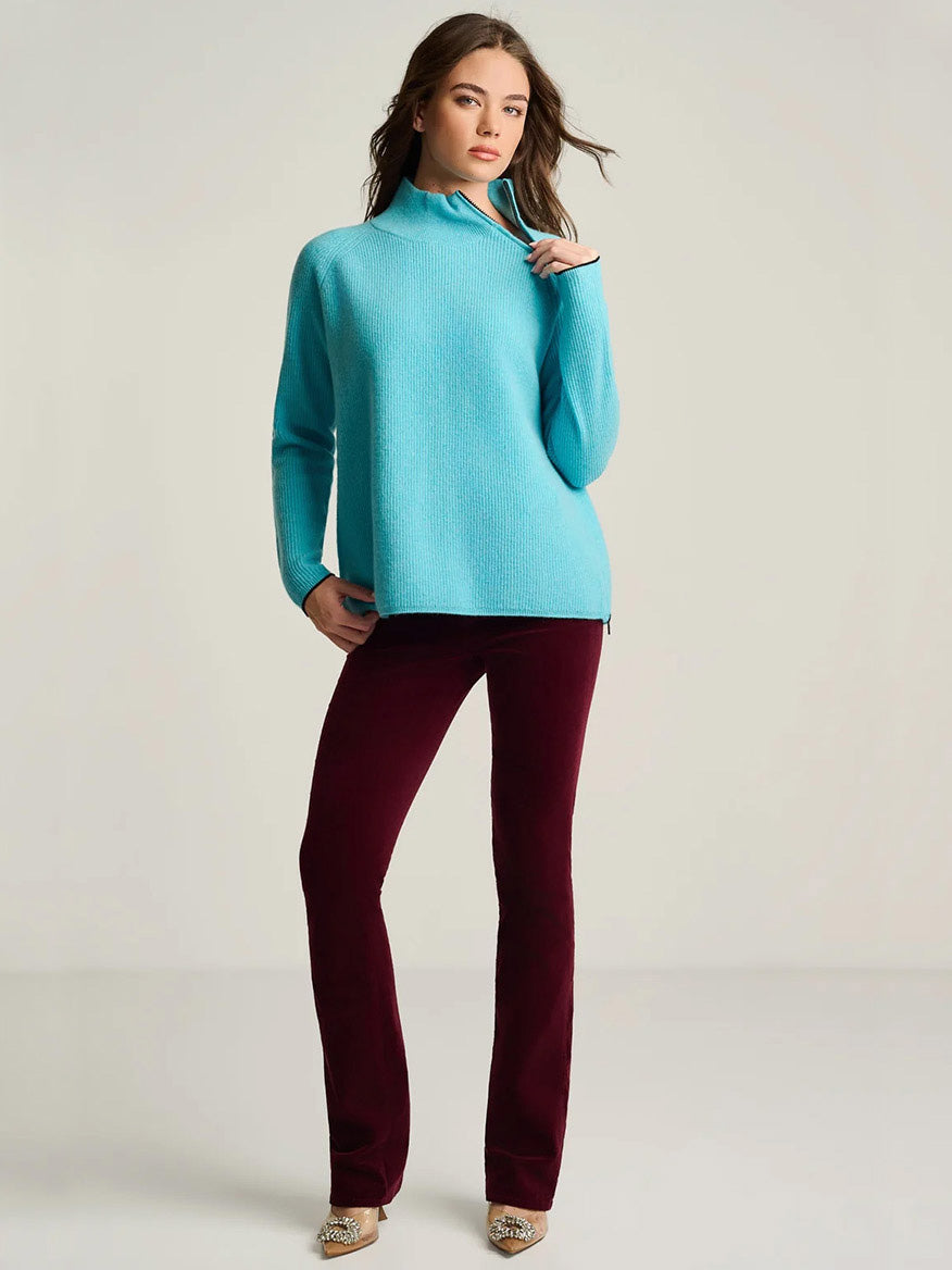 The Lisa Todd Double Trouble Cashmere Sweater in Blue Magic, a bright blue knit with a quarter-zip mock neck and rib stitching, worn with dark red trousers.