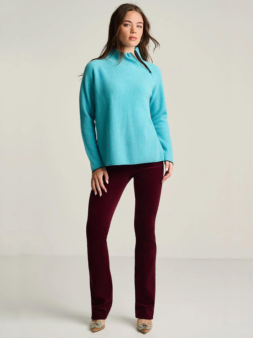 A woman wearing a Lisa Todd Double Trouble Cashmere Sweater in Blue Magic with a contrast zip neckline and dark maroon trousers.