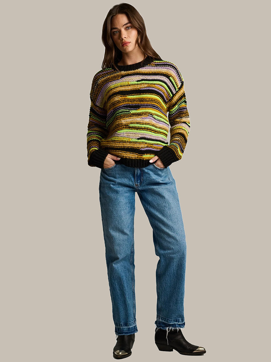 A person wears a Lisa Todd Fillati Sweater in Black Multi, a chunky alpaca mohair knit with horizontal stripes, paired with blue jeans and black boots.