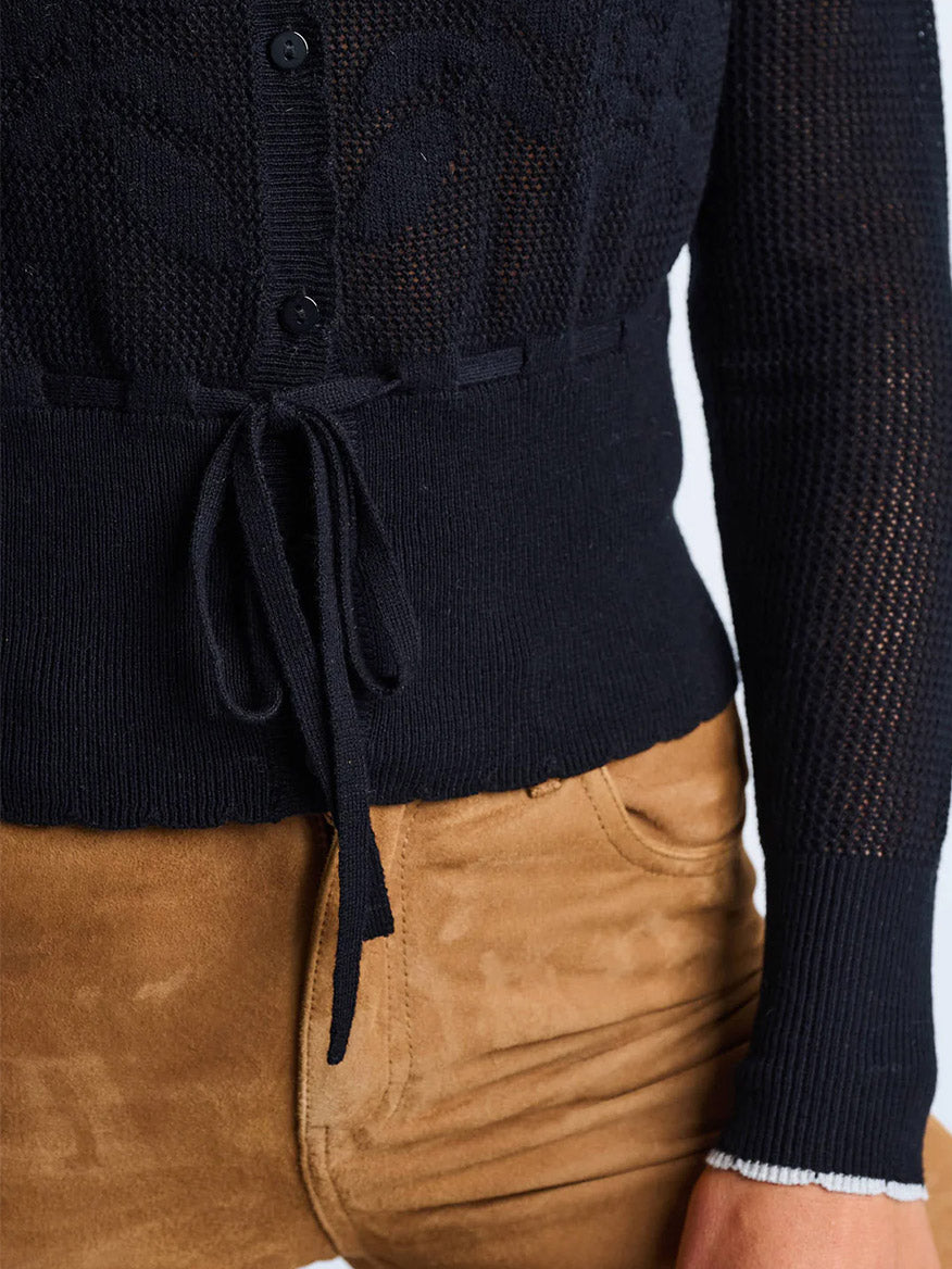 Someone is wearing the Lisa Todd Flirt Cardigan in Black with a tied waist, paired with light brown suede pants.