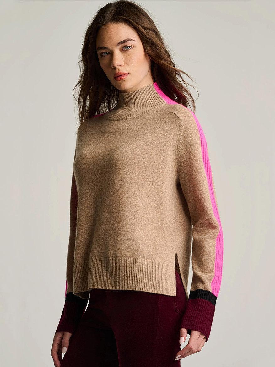 Woman wearing a Lisa Todd High Spirits Mock in Biscuit with pink and black striped sleeves and dark red pants, standing against a plain light background.