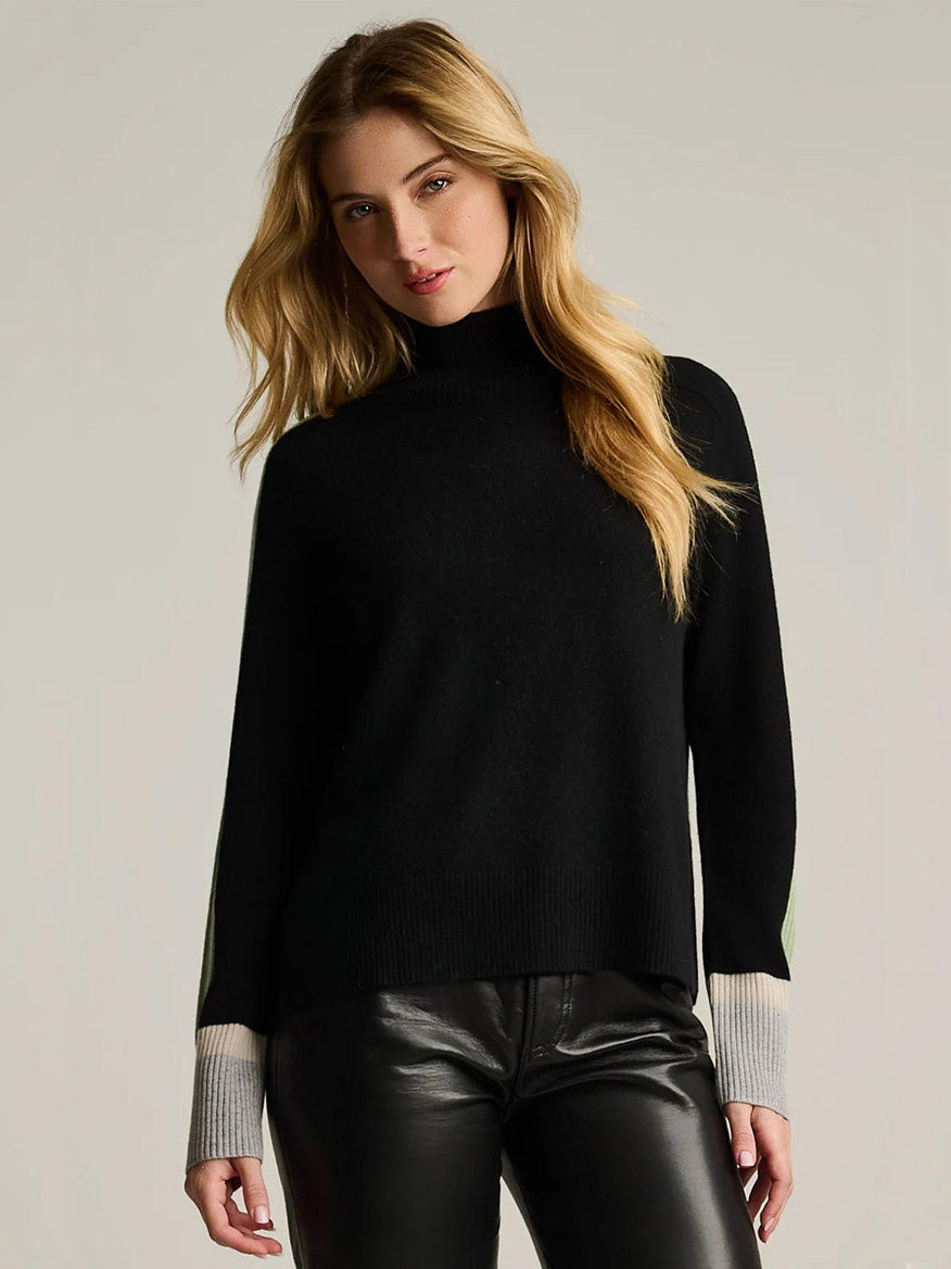 Lisa Todd High Spirits Mock in Onyx: a black mock-neck sweater in a relaxed raglan silhouette with long sleeves featuring striped cuffs in light green, white, and gray.