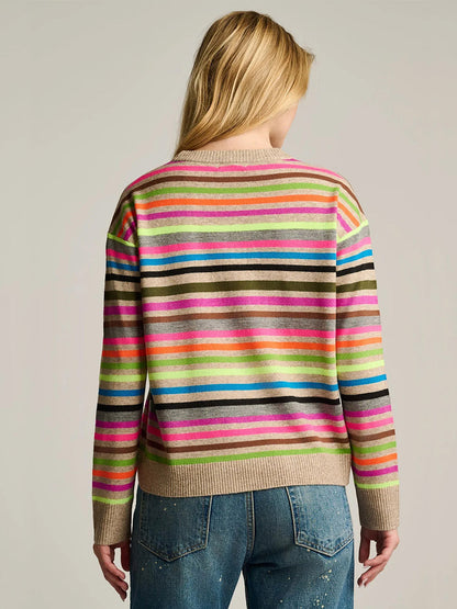 Person with long blonde hair shown from behind, wearing the Lisa Todd Hype The Stripe Sweater in Oat Multi Stripe and blue paint-splattered jeans against a plain background.