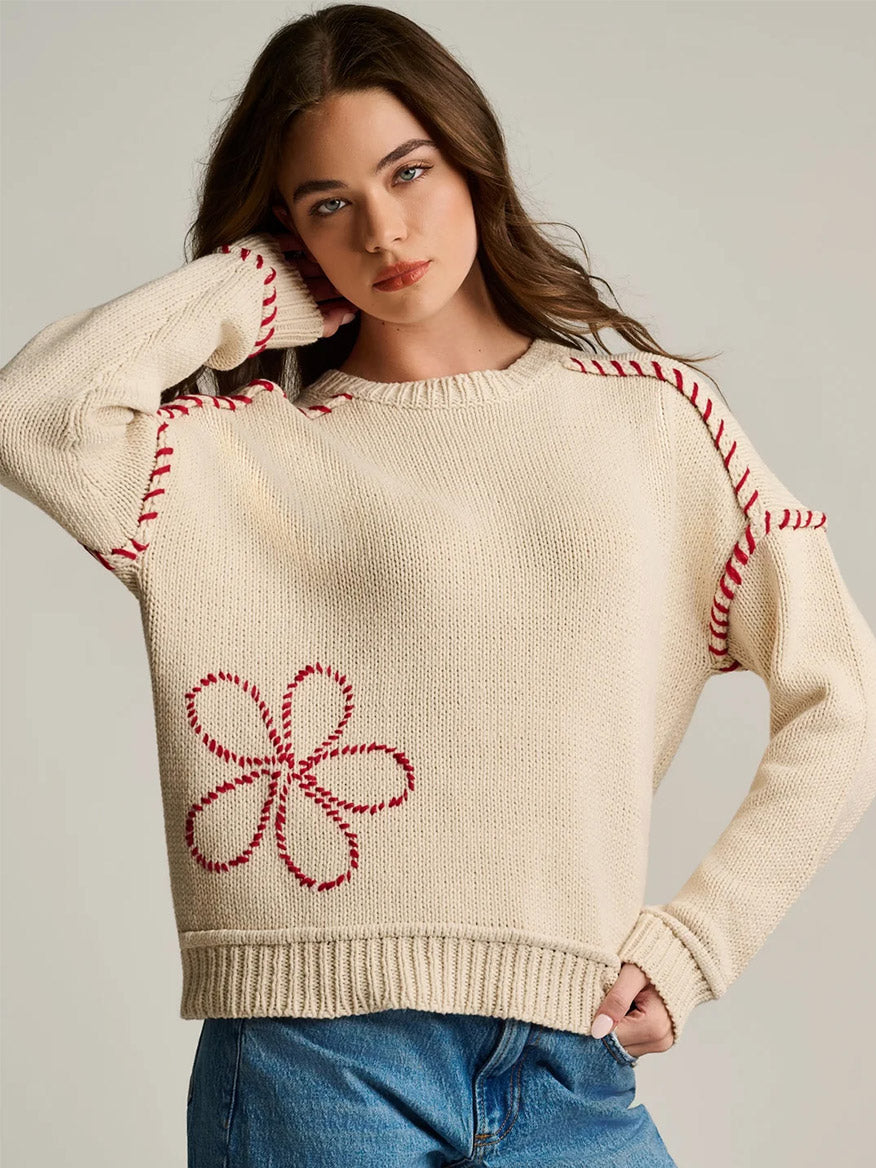 Woman wearing the Lisa Todd In Bloom Sweater in Salty—cream knit with red stitching and floral pattern—paired with blue jeans against a neutral background.