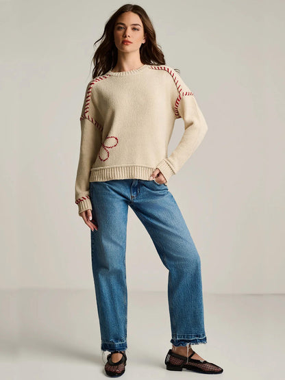 A person stands against a plain background wearing the Lisa Todd In Bloom Sweater in Salty, blue jeans, and black shoes.