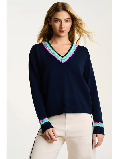 Woman wearing the Lisa Todd In The Mix Sweater in Navy, a relaxed V-neck knit with multicolored pink, green, and blue trim on the neckline and cuffs, styled with light-colored pants.