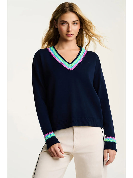 Woman wearing the Lisa Todd In The Mix Sweater in Navy, a relaxed V-neck knit with multicolored pink, green, and blue trim on the neckline and cuffs, styled with light-colored pants.