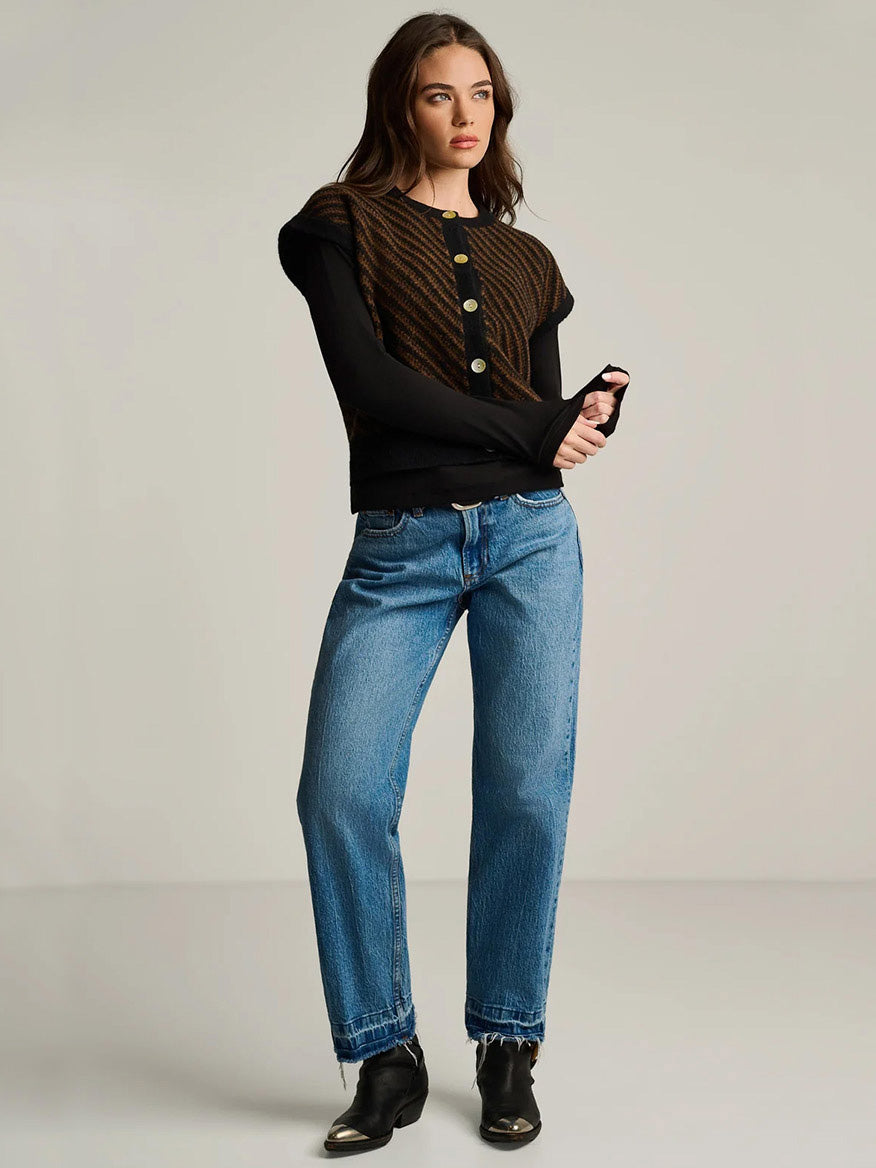 A person wearing a Lisa Todd In Vest in Black Combo over a black long-sleeve top, blue jeans, and black ankle boots with metallic toe caps.