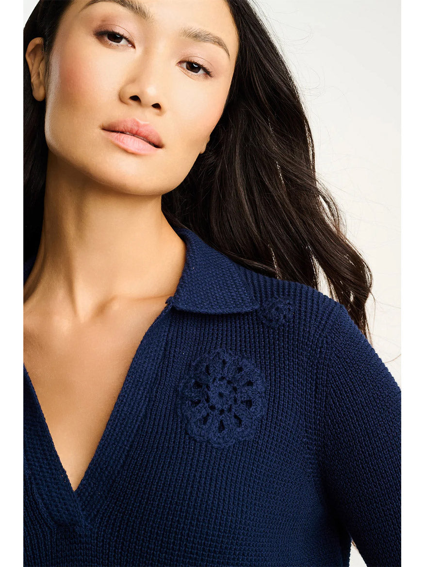 A woman with long dark hair wears the Lisa Todd Knit Bliss Cotton Sweater in Navy, featuring hand-crocheted medallions near the collar and made from 100% cotton.
