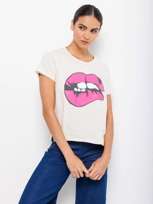 Woman posing in a white Lisa Todd Love Bites Tee in Bluff with a pink lips graphic, paired with blue jeans featuring raw hems.