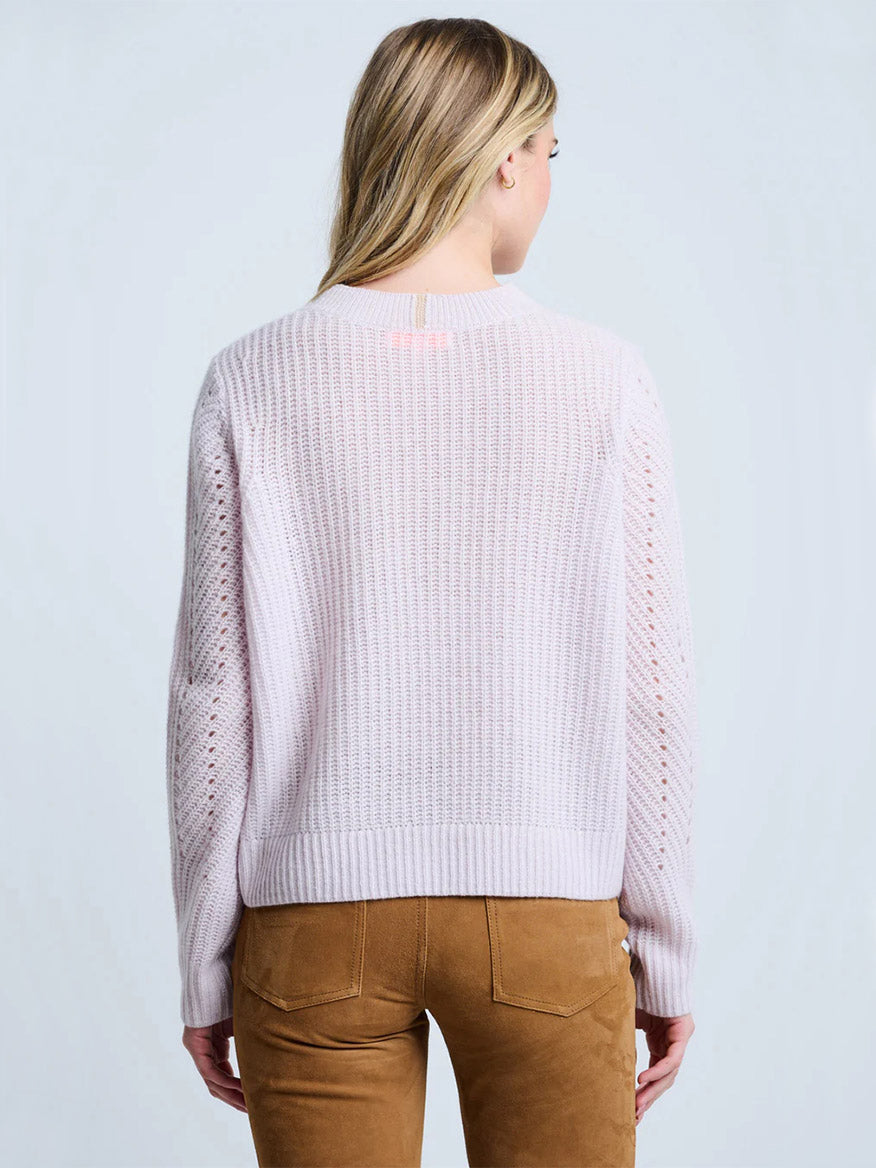 A person stands with their back to the camera, wearing the Lisa Todd Luxe Softie Sweater in Lotus—a relaxed fit, light pink cashmere crewneck—paired with tan pants against a plain light background.