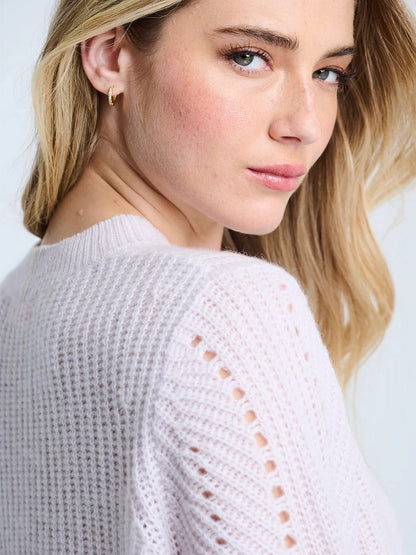 A woman with long blonde hair models the Lisa Todd Luxe Softie Sweater in Lotus, a relaxed fit light pink ribbed sweater, as she looks over her shoulder toward the camera.