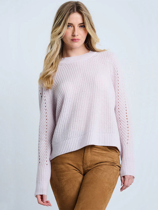 A woman with long blonde hair wears the Lisa Todd Luxe Softie Sweater in Lotus, a relaxed fit light pink ribbed sweater, with tan pants against a plain light background.