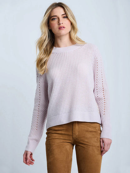 A woman with long blonde hair wears the Lisa Todd Luxe Softie Sweater in Lotus, styled in a relaxed fit, along with tan pants against a plain light background.
