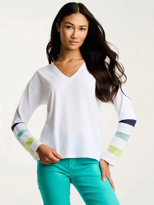 Woman wearing the Lisa Todd Mesh Fest Cotton Tee in White, featuring colored sleeve stripes and teal pants, standing against a plain light background.
