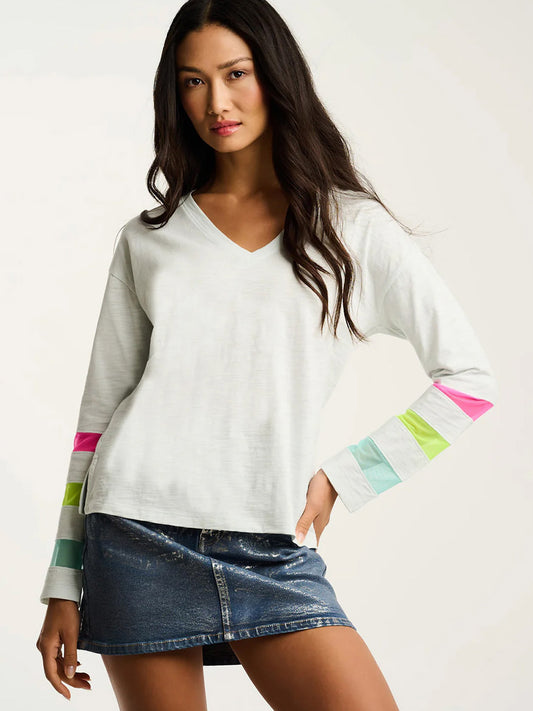 Woman wearing the Lisa Todd Mesh Fest Cotton Tee in Salty Air, a relaxed fit, lightweight cotton top with colorful striped sleeves, paired with a blue denim skirt against a plain background.